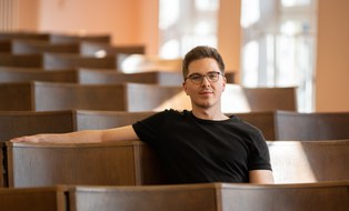 Aymeric Benken sitzt im Hörsaal und blickt in die Kamera