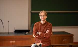 Nils Imhof steht im Hörsaal vor der Tafel und blickt in die Kamera
