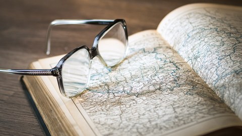 The picture shows a pair of glasses lying on an open book.