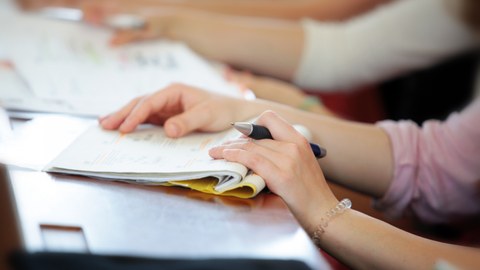 Das Bild zeigt eine Studierende im Hörsaal mit einem Stift und Notizbuch in der Hand.