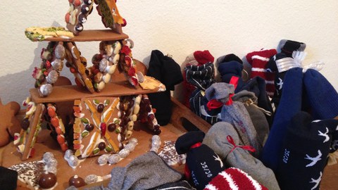 Das Bild zeigt ein Pfefferkuchenhaus sowie Socken, die als Adventskalender genutzt werden. 