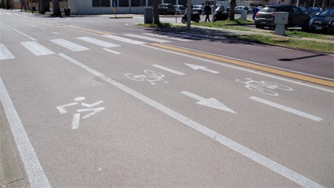 Das Bild zeigt eine Straße in Quartu Sant'Elena, Sardinien. Im Vordergrund wurde ein breiter Fahrbahnstreifen für Läufer abmarkiert. Darauf folgt ein Radfahrstreifen und im Hintergrund eine Fahrspur für den Kfz-Verkehr (Einbahnstraßenregelung). 