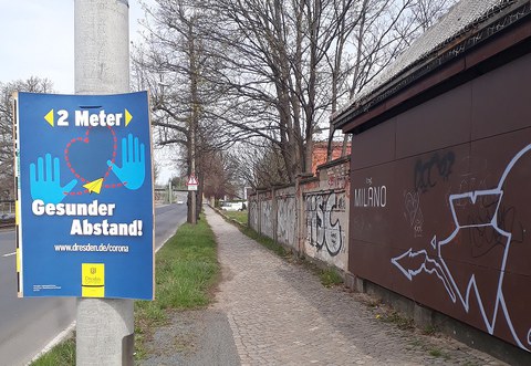 Poster by the City of Dresden raising awareness to keep a "healthy" distance of 2 meters due to Covid-19, while the sidewalk does not allow pedestrians to keep such a distance.