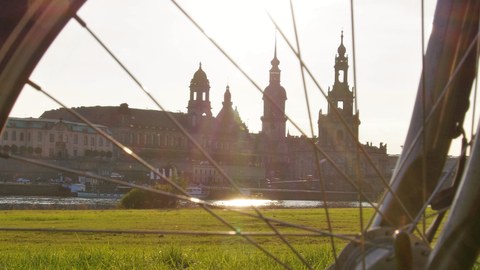 Dargestellt ist eine Silhouette von Dresden (Frauenkirche, Hofkirche) sowie im Vordergrund ein Fahrrad (Deteil des Rads)