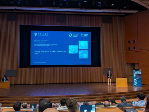 Prof. Dr.-Ing. Günther Prokop hält auf der AVEC 2026 in Tsukuba seine Keynote. Hinter ihm ist die Titelfolie „Driving Simulation – Take it to the Next Level“ zu sehen.