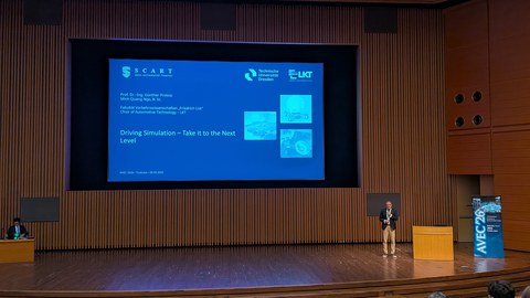 Prof. Dr.-Ing. Günther Prokop hält auf der AVEC 2026 in Tsukuba seine Keynote. Hinter ihm ist die Titelfolie „Driving Simulation – Take it to the Next Level“ zu sehen.