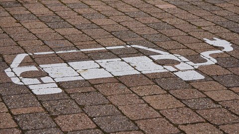 gekennzeichneter Parkplatz für ein E-Auto zum Aufladen. Pflastersteine. Daauf ist mit weißer Farbe ein Auto mit einem Kabel gemalt.
