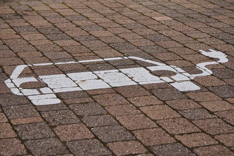 gekennzeichneter Parkplatz für ein E-Auto zum Aufladen. Pflastersteine. Daauf ist mit weißer Farbe ein Auto mit einem Kabel gemalt.