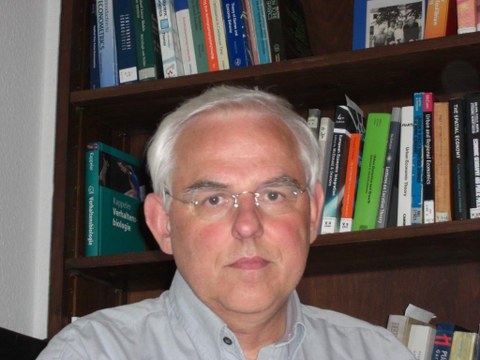 Porträt von Prof. Johannes Bröcker. Er sitz vor einem Bücherregal.