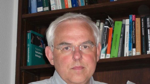 Porträt von Prof. Johannes Bröcker. Er sitz vor einem Bücherregal.