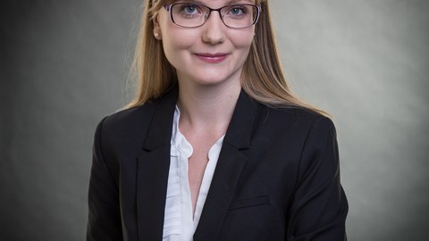 Porträt einer lächelnden Frau mit glatten langen Haaren, Pony, schwarzem Blazer und weißer Bluse drunter.