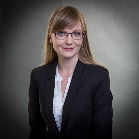 Porträt einer lächelnden Frau mit glatten langen Haaren, Pony, schwarzem Blazer und weißer Bluse drunter.