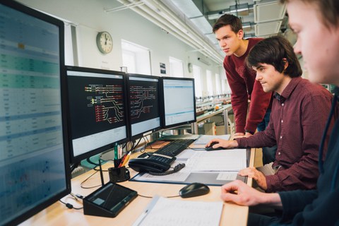 3 junge Männer schauen auf Monitore