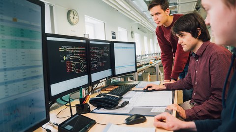 3 junge Männer schauen auf Monitore