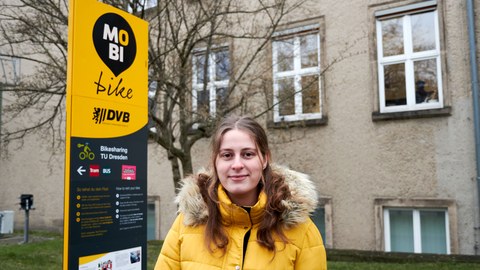 Eine junge Frau in gelber Jacke steht vor einem MobiPunkt in Dresden