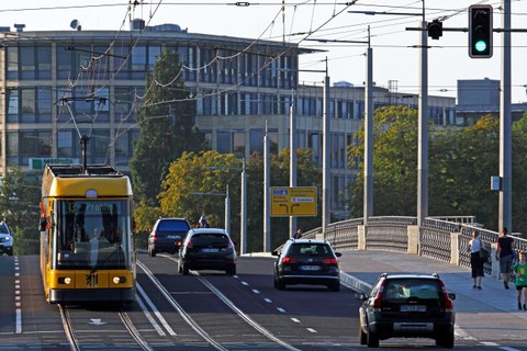 Stadtverkehr in Dresden, eine Straßenbahn fährt auf einer Brücke daneben Autos und auf dem Fußweg Personen