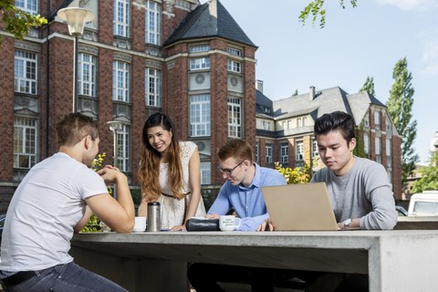 vier internationale Studierende sitzen vor der Biomensa mit Laptop. Sie unterhalten sich und lernen.