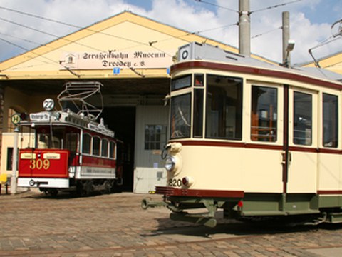 Vor einem Gebäude stehen 2 historische Straßenbahnen. 