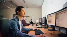 Drei Studierende sitzen nebeneinander an Bildschirmarbeitsplätzen.