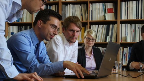 Vier Personen betrachten den Monitor eines Laptops