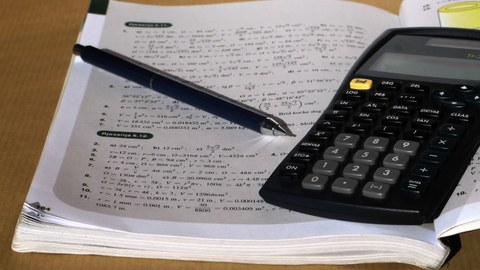 Picture of an opened exercise book together with a calculator and a pen