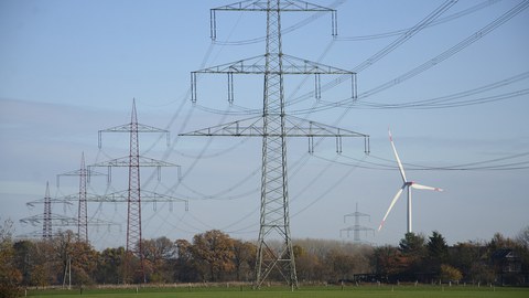 Hochspannungsleitung mit Windrad im Hintergrund