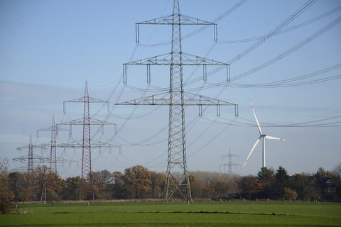 Hochspannungsleitung mit Windrad im Hintergrund