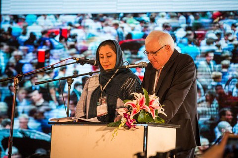 A man and a woman with a headscarf stand at a lectern and give a speech. 