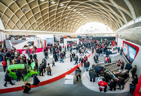 View into an exhibition hall with cars and visitors. 