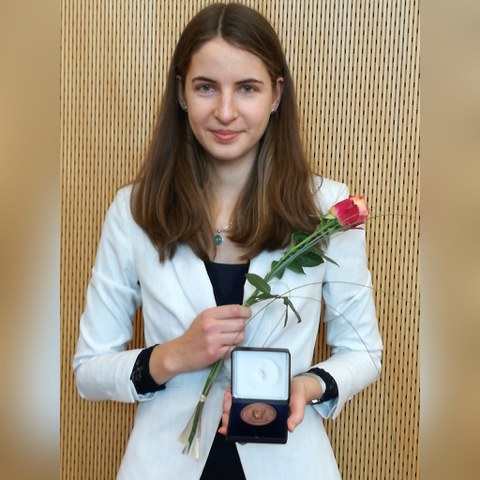 Eine Frau (Maria Beranek) mit einer Medaille in einer Schatulle und einer Rose in der Hand. 