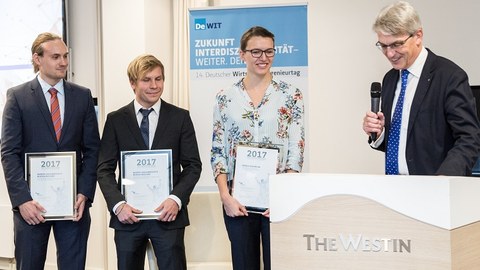 Presentation of the VWI Graduation Award. 3 persons holding a certificate in their hands. The person on the right side speaks and holds a microphone in his hand.