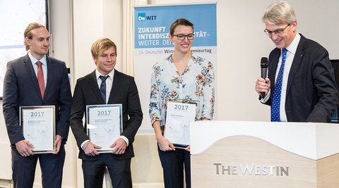 Presentation of the VWI Graduation Award. 3 persons holding a certificate in their hands. The person on the right side speaks and holds a microphone in his hand.