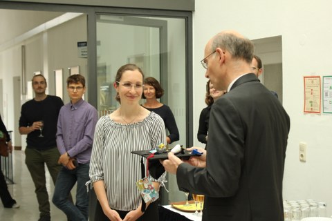 Prof. Udo Buscher presents Kirsten Hoffmann with her doctoral degree. In the background there are more people.