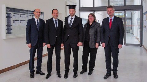5 people wearing suits. The man in the middle is wearing a doctor's hat.