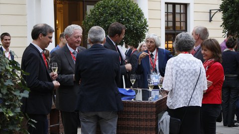 Several people are standing at tables outside and talking to each other.