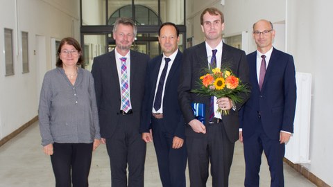 5 persons in suits. The 2nd man from the right holds a bouquet of flowers in his hand