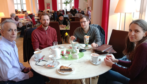 4 Personen sitzen an einem runden Tisch in einem Café.