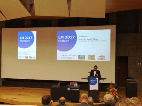 A man holding a presentation. In the background there is a beamer projection. 