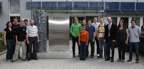 Exkursionsteam vor dem Werksgelände der SolarWord AG. In der Mitte befindet sich eine Informationstafel.