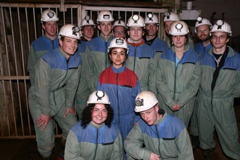 Exkursionsteam mit Sicherheitskleidung und Sicherheitshelmen vor dem Fahrstuhl des Bergwerkes.