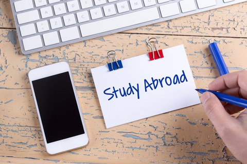 Das Foto zeigt einen Tisch. Darauf liegt eine Computertastatur, ein Handy und ein Notizzettel mit der Aufschrift "Study Abroad".