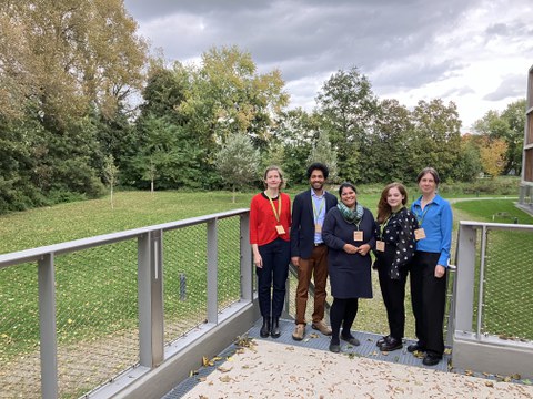Team members of the junior professorship stand smiling in the greenery in front of the event building
