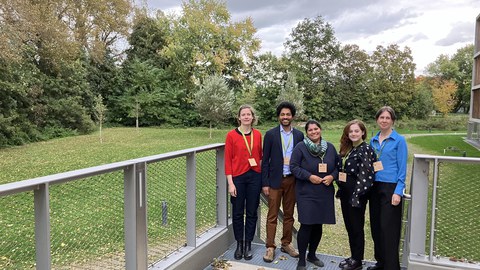Teammitglieder der Juniorprofessur stehen lächelnd im Grünen vor dem Veranstaltungsgebäude