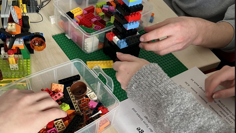 Hände bauen mit Lego® Steinen einen Turm, ringsum liegen weitere Lego®-Steine und -Platten.