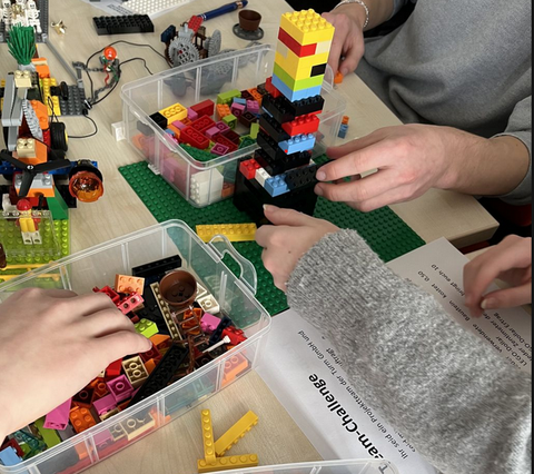 Hände bauen mit Lego® Steinen einen Turm, ringsum liegen weitere Lego®-Steine und -Platten.