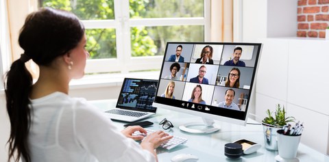 Foto: Eine Frau an ihrem Arbeitsplatz, die online in einer Videokonferenz mit neun Kollegen spricht.