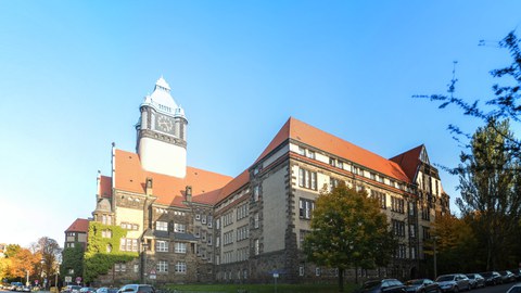 Das Foto zeigt die Außenansicht des Georg-Schumann-Baus der TU Dresden. Charakteristisch ist der Wehrturm und das burgähnliche Aussehen des Gebäudes.