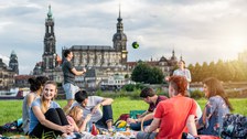 Group of students at the Elbe. They play volleyball and sit chatting on the lawn.