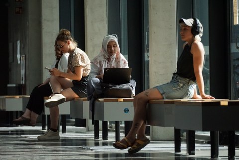 Fotos von vier Personen, die auf dem Campus der TU Dresden auf Bänke sitzend etwas anhören oder auf den Laptop oder das Handy schauen. 