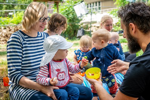 Das Bild zeigt Kleinkinder mit ihren Eltern im Kindergarten "Campusnest" beim Obst essen.